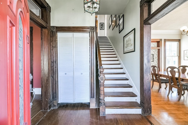 staircase featuring wood-type flooring, a notable chandelier, and ornamental molding