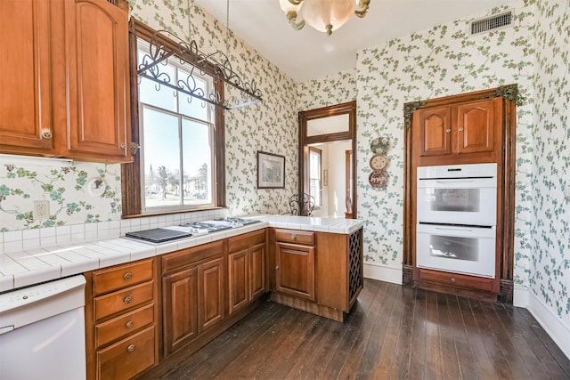 kitchen with tile countertops, kitchen peninsula, white appliances, and dark wood-type flooring