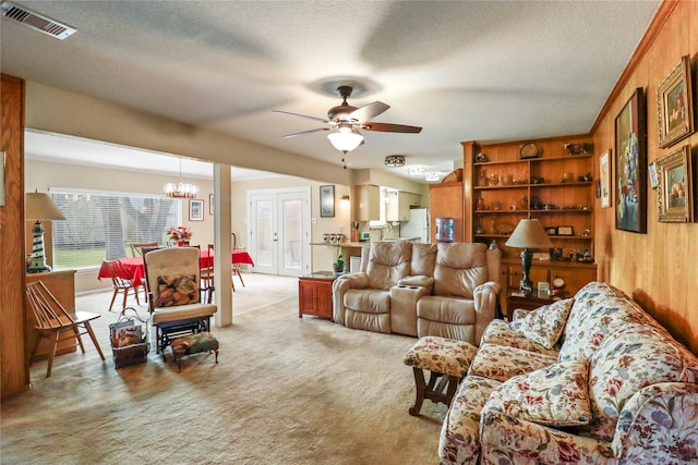 carpeted living room with a textured ceiling, ceiling fan with notable chandelier, and wood walls