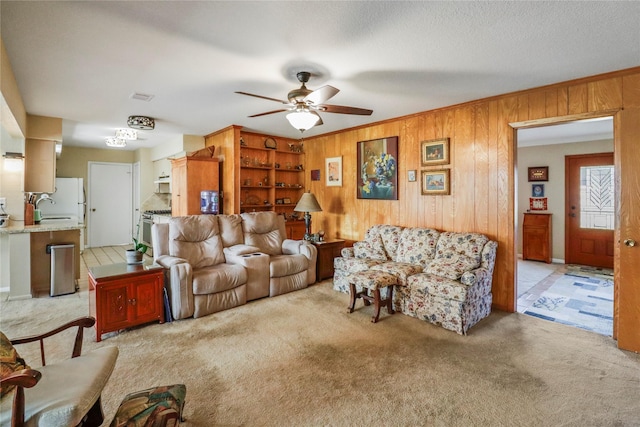 living room featuring light carpet, ceiling fan, wood walls, and sink