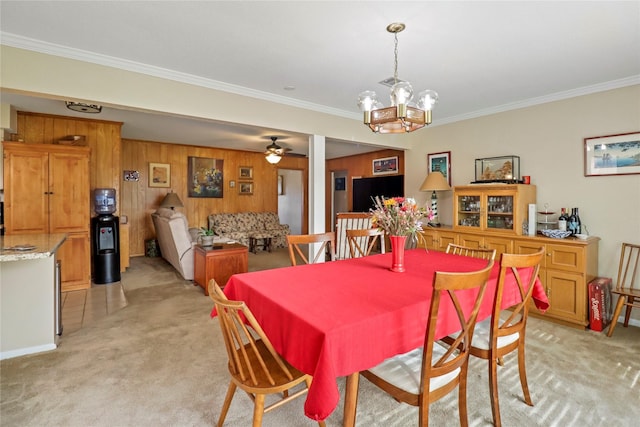 carpeted dining room with ceiling fan with notable chandelier, crown molding, and wooden walls