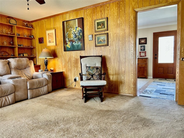 sitting room featuring ceiling fan, wooden walls, ornamental molding, and carpet flooring