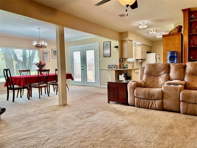 living room with visible vents, ornamental molding, ceiling fan with notable chandelier, french doors, and light colored carpet