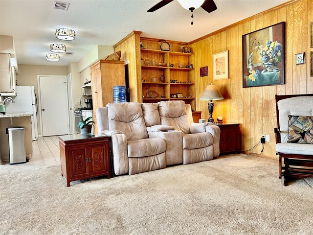 living area featuring light carpet, visible vents, a ceiling fan, and wooden walls