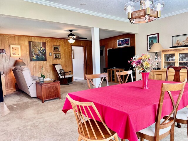 carpeted dining space with ceiling fan, wood walls, and ornamental molding