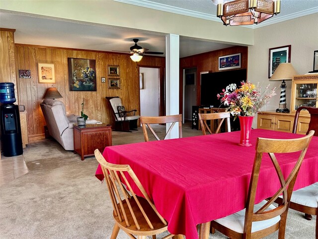 carpeted dining room with wooden walls, a ceiling fan, and ornamental molding