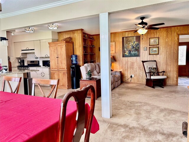 dining space with a ceiling fan, light carpet, wooden walls, and crown molding