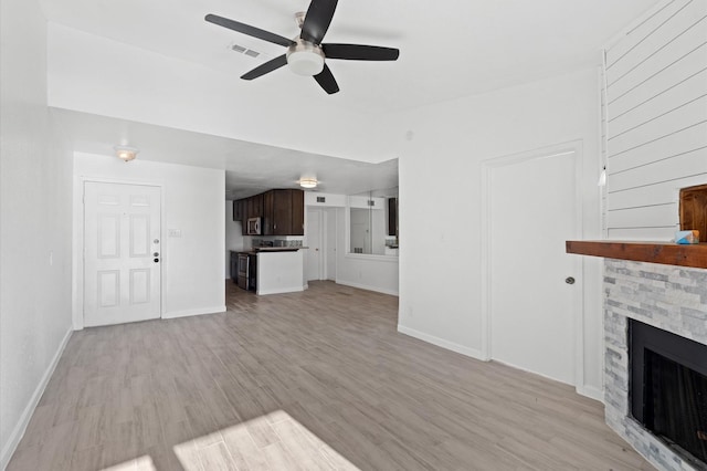 unfurnished living room featuring ceiling fan, a fireplace, and light wood-type flooring