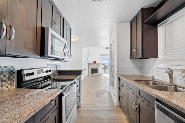 kitchen with a fireplace, dark brown cabinetry, sink, and appliances with stainless steel finishes