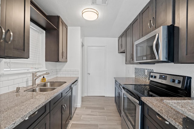 kitchen featuring sink, light stone counters, light hardwood / wood-style flooring, dark brown cabinets, and appliances with stainless steel finishes