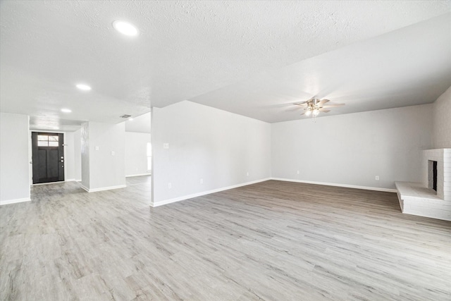 unfurnished living room featuring ceiling fan, light hardwood / wood-style floors, a textured ceiling, and a brick fireplace