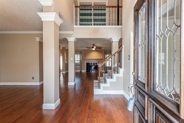 entrance foyer featuring ornate columns, a textured ceiling, ornamental molding, dark hardwood / wood-style flooring, and ceiling fan