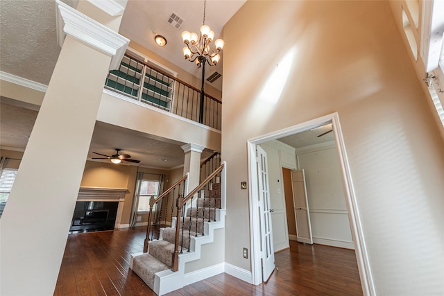 staircase with hardwood / wood-style flooring, crown molding, ceiling fan with notable chandelier, and a high ceiling