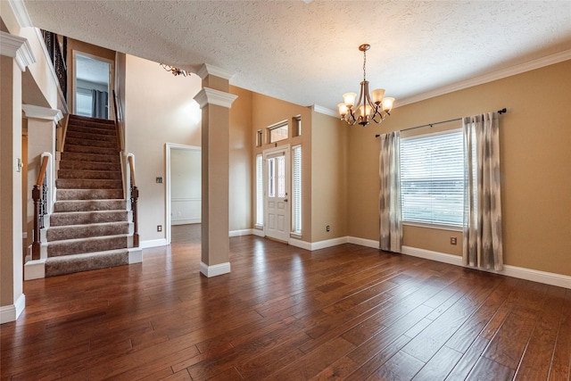 entrance foyer with dark hardwood / wood-style floors, decorative columns, a chandelier, ornamental molding, and a textured ceiling