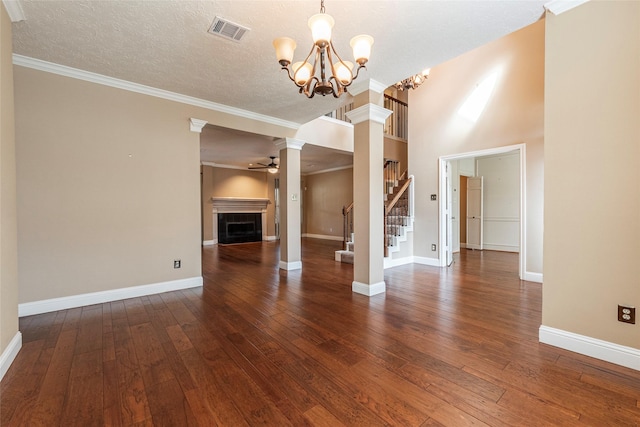 unfurnished living room featuring ceiling fan with notable chandelier, a fireplace, decorative columns, dark wood-type flooring, and a textured ceiling