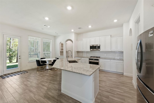 kitchen featuring white cabinets, a center island with sink, sink, light stone counters, and stainless steel appliances