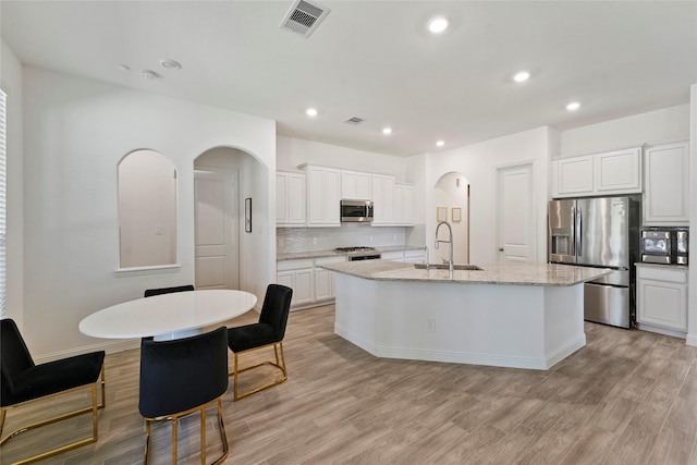 kitchen with appliances with stainless steel finishes, light wood-type flooring, sink, a center island with sink, and white cabinetry