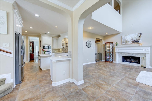 kitchen featuring kitchen peninsula, appliances with stainless steel finishes, ornamental molding, white cabinetry, and a tiled fireplace