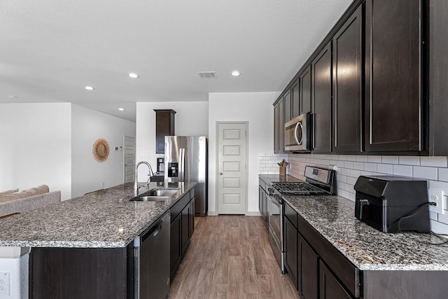 kitchen featuring sink, stainless steel appliances, dark stone counters, wood-type flooring, and decorative backsplash