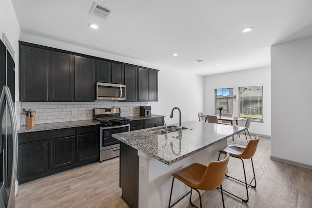 kitchen with light stone countertops, a kitchen breakfast bar, stainless steel appliances, sink, and a center island with sink