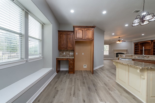 kitchen with light stone countertops, hanging light fixtures, light hardwood / wood-style floors, tasteful backsplash, and sink