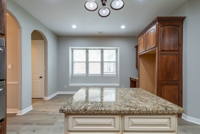 kitchen with a kitchen island, light wood-type flooring, and light stone counters