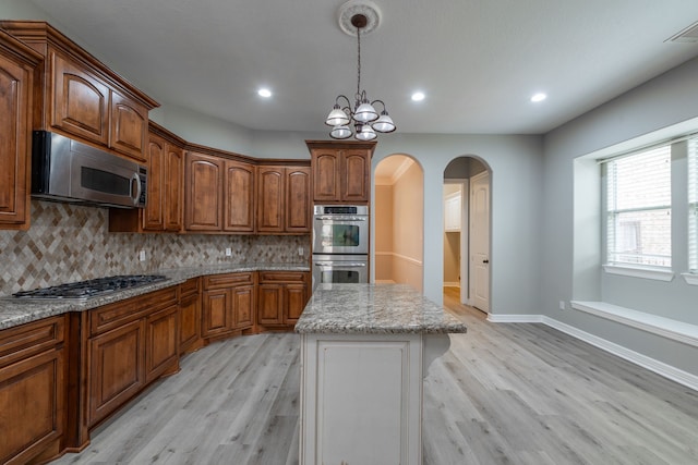 kitchen featuring stainless steel appliances, a kitchen island, backsplash, and a notable chandelier