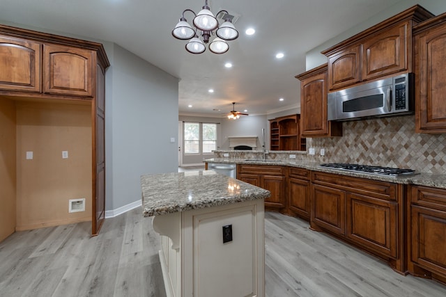 kitchen with a center island, decorative light fixtures, backsplash, ceiling fan with notable chandelier, and appliances with stainless steel finishes