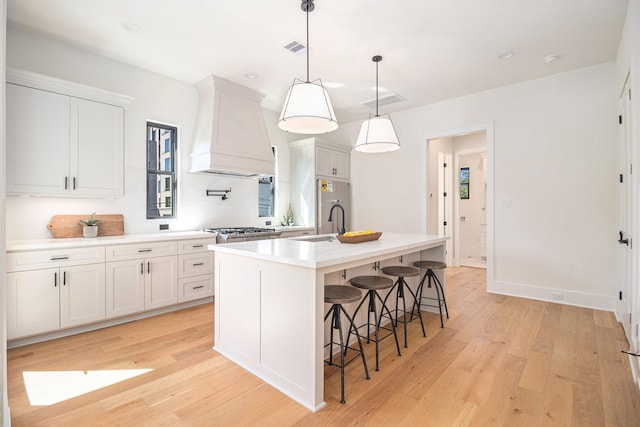 kitchen featuring decorative light fixtures, white cabinets, an island with sink, and custom range hood