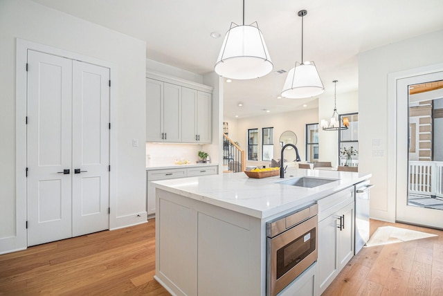 kitchen with built in microwave, sink, hanging light fixtures, a kitchen island with sink, and white cabinets