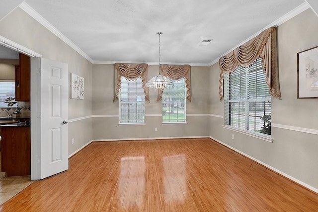 unfurnished dining area with hardwood / wood-style floors, crown molding, and an inviting chandelier