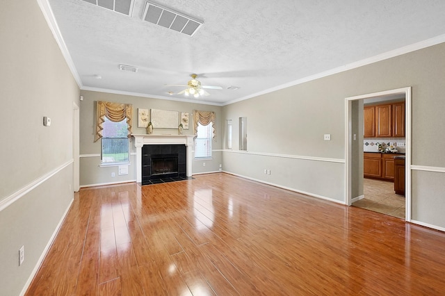 unfurnished living room with ceiling fan, light hardwood / wood-style floors, a tile fireplace, and ornamental molding