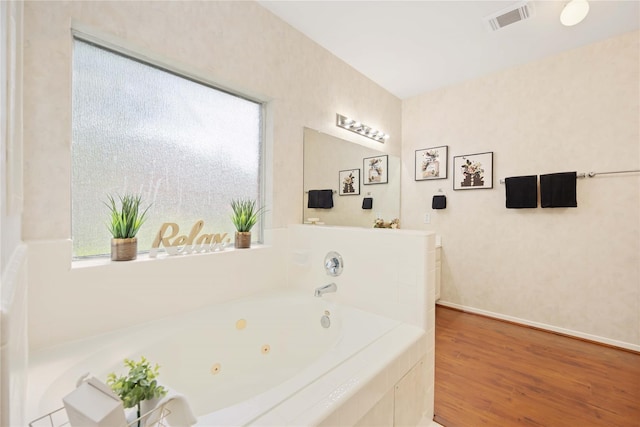 bathroom featuring a relaxing tiled tub, wood-type flooring, and plenty of natural light