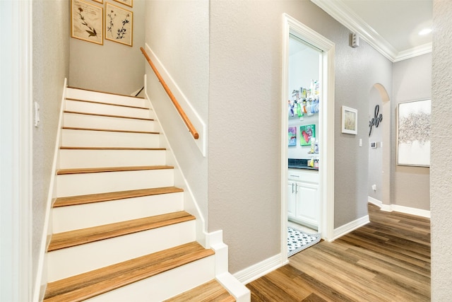 staircase with wood-type flooring and ornamental molding