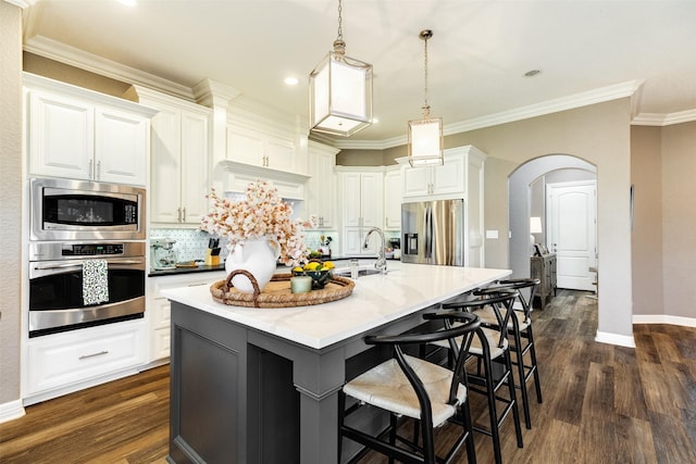 kitchen featuring stainless steel appliances, white cabinetry, a kitchen island with sink, and decorative light fixtures