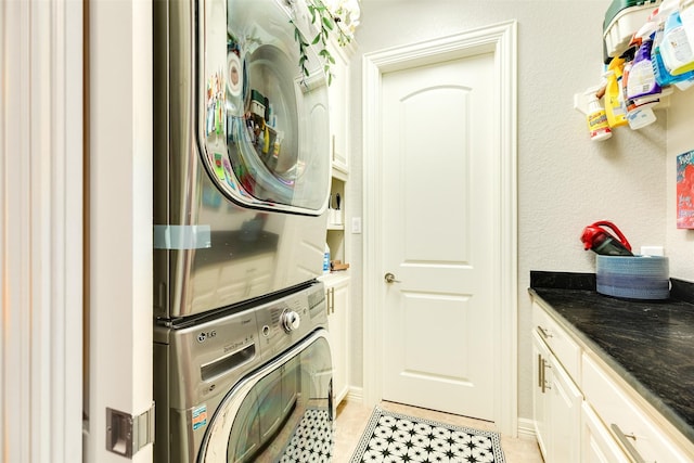 washroom featuring stacked washer and dryer, cabinets, and light tile patterned flooring