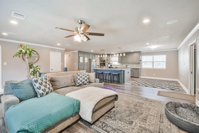 living room with ceiling fan, ornamental molding, and light wood-type flooring