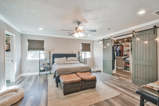 bedroom with ceiling fan, a spacious closet, a barn door, crown molding, and a closet