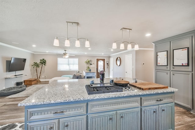 kitchen with pendant lighting, a center island, crown molding, ceiling fan, and stainless steel gas cooktop