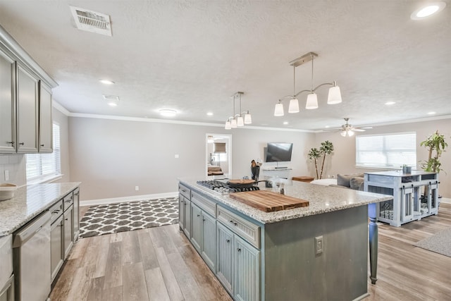 kitchen with ceiling fan, a center island, stainless steel appliances, light stone counters, and pendant lighting