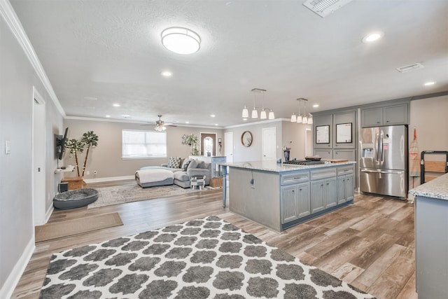 kitchen featuring ceiling fan, hanging light fixtures, stainless steel appliances, a center island with sink, and hardwood / wood-style flooring