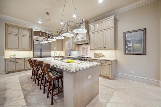 kitchen featuring light stone counters, ornamental molding, stainless steel built in refrigerator, and a kitchen island with sink