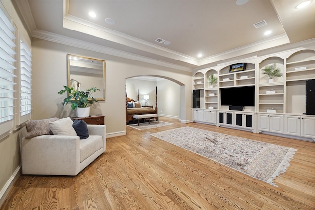 living room featuring a raised ceiling, built in features, ornamental molding, and light hardwood / wood-style flooring