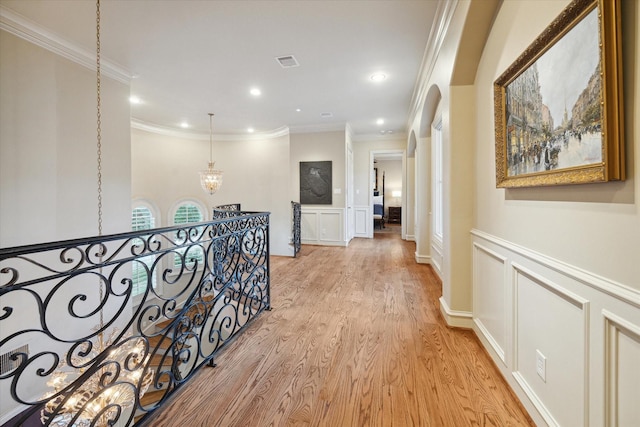 hall with light hardwood / wood-style floors, crown molding, and an inviting chandelier