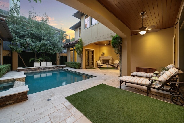 pool at dusk featuring an in ground hot tub, a patio, an outdoor hangout area, and ceiling fan