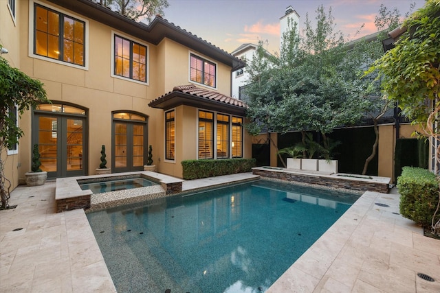 back house at dusk featuring a swimming pool with hot tub, a patio, and french doors