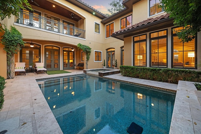 pool at dusk featuring a patio area, an in ground hot tub, and french doors