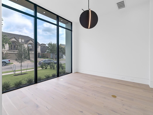 unfurnished room with floor to ceiling windows and light hardwood / wood-style flooring