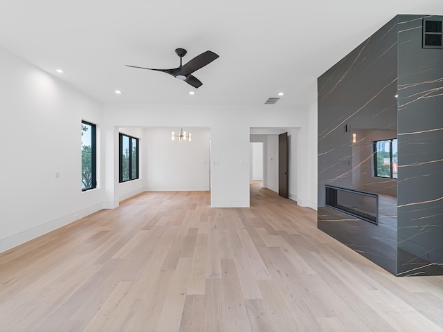 unfurnished living room with ceiling fan with notable chandelier and light wood-type flooring