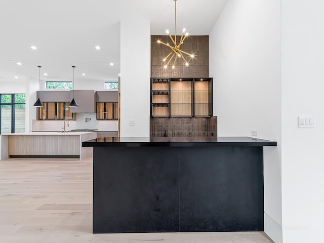 kitchen featuring sink, hanging light fixtures, an inviting chandelier, kitchen peninsula, and light wood-type flooring